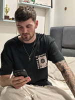 Load image into Gallery viewer, Model sporting the House of SwaSha Honor and Harmony t-shirt, sitting on a bed using a phone. Casual comfort, sustainable fashion.