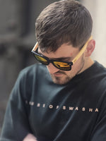 Load image into Gallery viewer, Close-up of model wearing House of SwaSha t-shirt and sunglasses with a blurred background