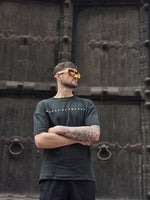 Load image into Gallery viewer, House of SwaSha hunter green oversized men’s t-shirt front view on model, round neck half sleeves, 210 GSM organic cotton standing in front of a large wooden door