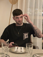 Load image into Gallery viewer, Detailed shot of the Honour and Harmony green oversized men’s t-shirt on a model at dinner table.