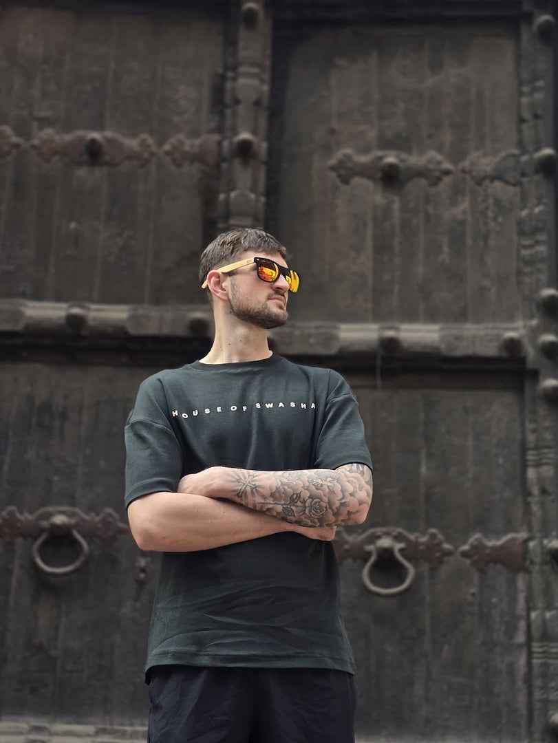 House of SwaSha hunter green oversized men’s t-shirt front view on model, round neck half sleeves, 210 GSM organic cotton standing in front of a large wooden door