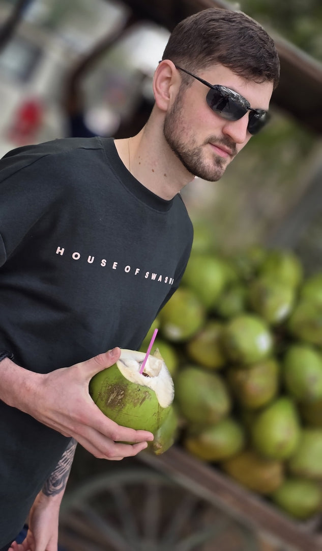 House of SwaSha hunter green oversized men’s t-shirt three-quarter front angle on model holding a green coconut with a straw. Everyday comfort and style