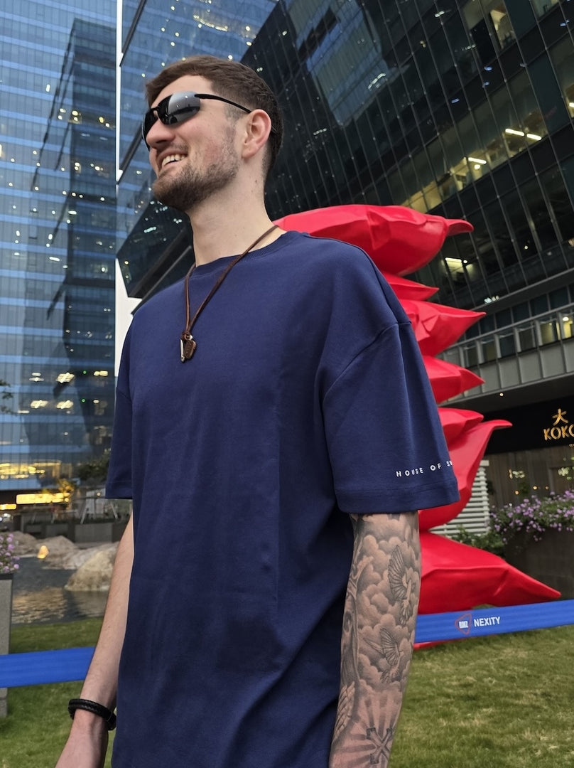 Model wearing a navy blue t-shirt with a cityscape background featuring modern buildings and red sculptures.